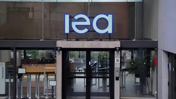 Glass entrance of the IEA building with large blue illuminated lettering and Energy Agency branding visible
