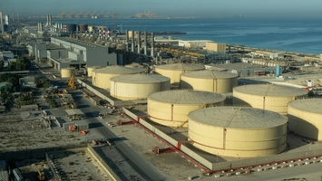 Aerial view of large cylindrical petroleum storage tanks at a coastal industrial facility near the sea